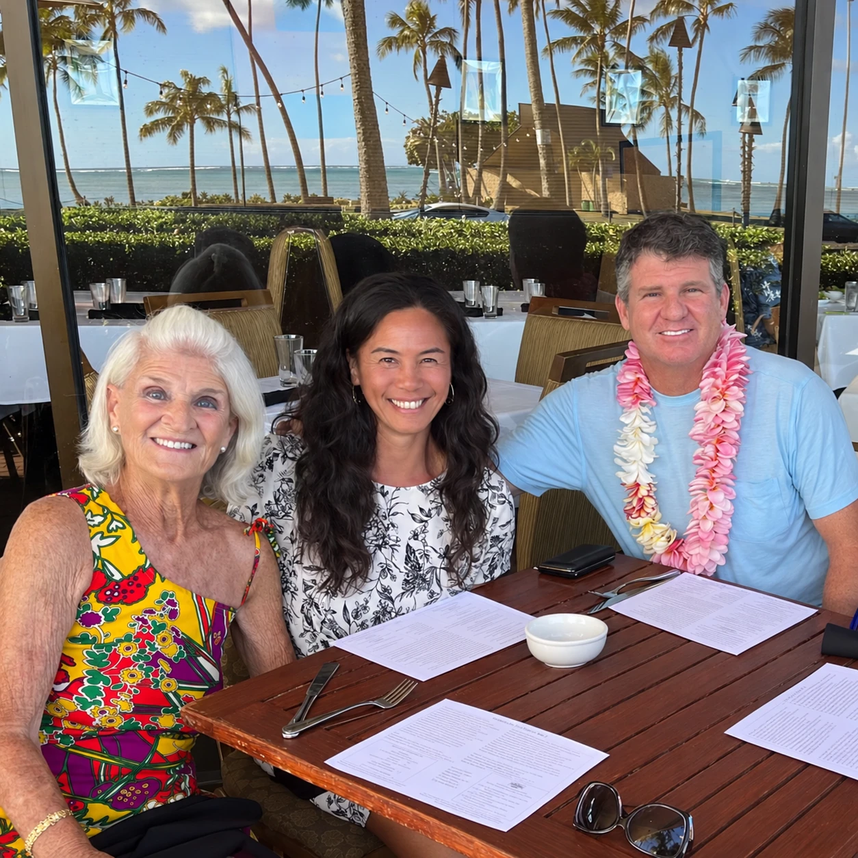 Shawn with his mother and wife, seated together at a restaurant by the ocean